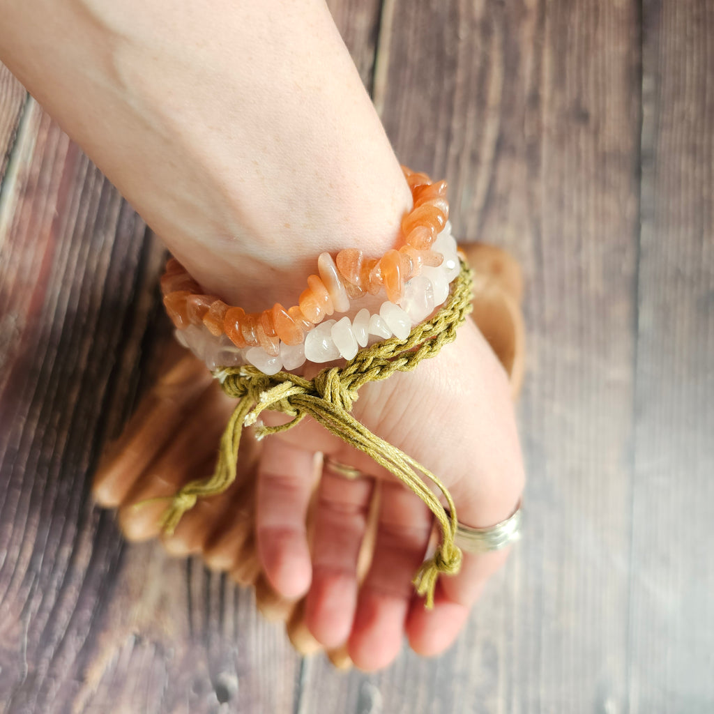 A sand-coloured crystal cord bracelet with an example crystal inside, on a wrist alongside other crystal chip bracelets 