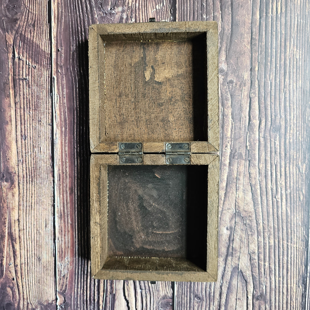 An open, empty square wooden box, placed on a wooden surface.