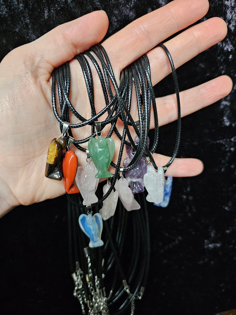 Several angel-shaped crystal pendant attached to black cord necklaces held in a person's hand on a dark background