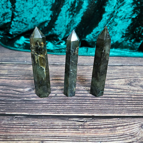 Three Labradorite general crystals stand side by side on a wooden surface. 