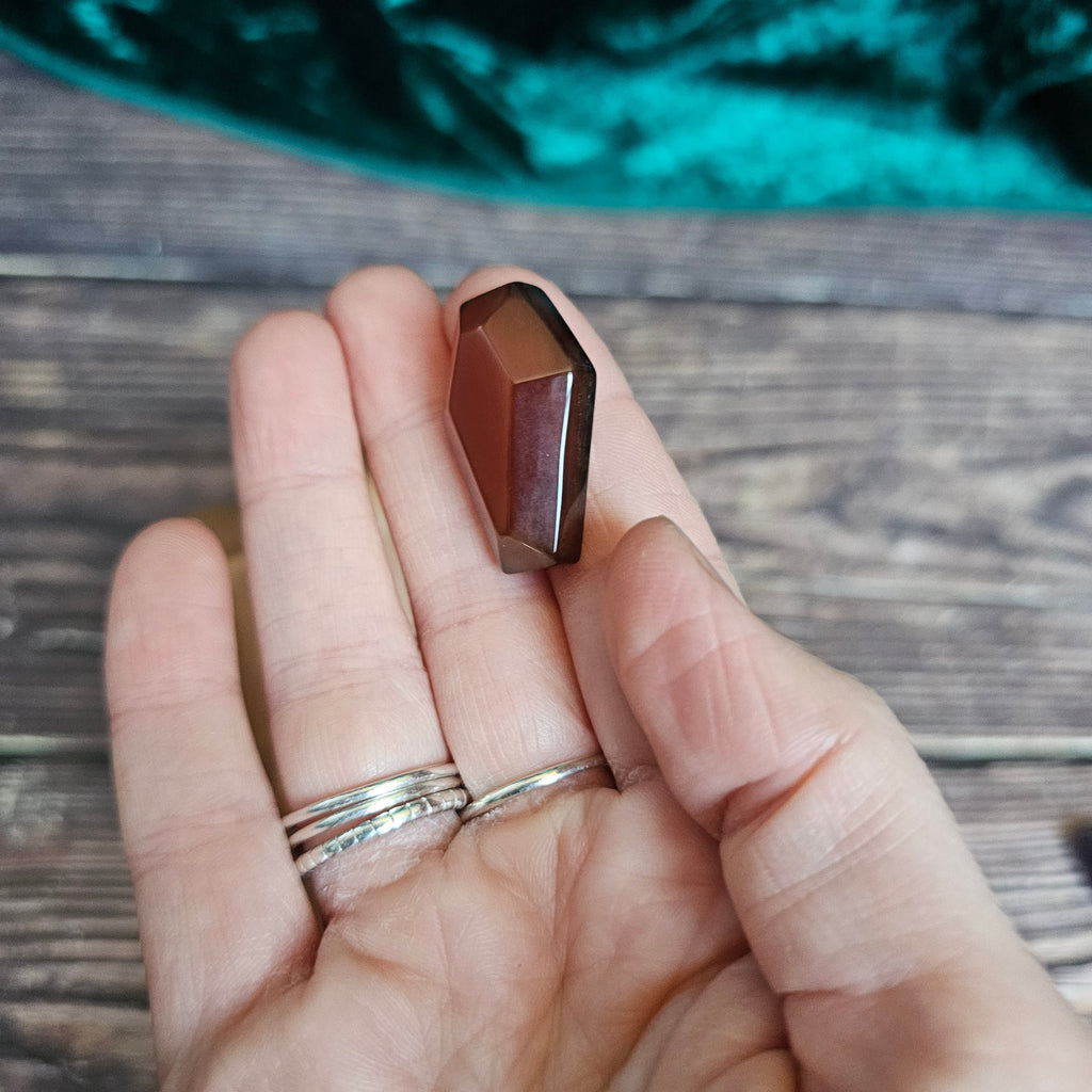 A red crystal shaped as a coffin is being held in someone's hand