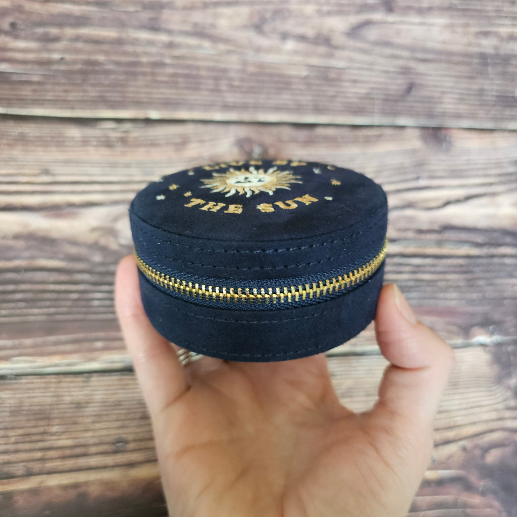 A person holding a closed navy blue round jewellery case.
