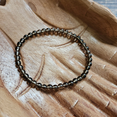 A beaded bracelet made of small, dark brown Smoky Quartz stones laid on a wooden surface.