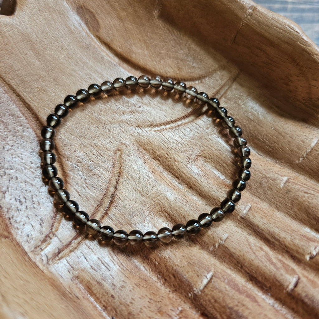 A beaded bracelet made of small, dark brown Smoky Quartz stones laid on a wooden surface.