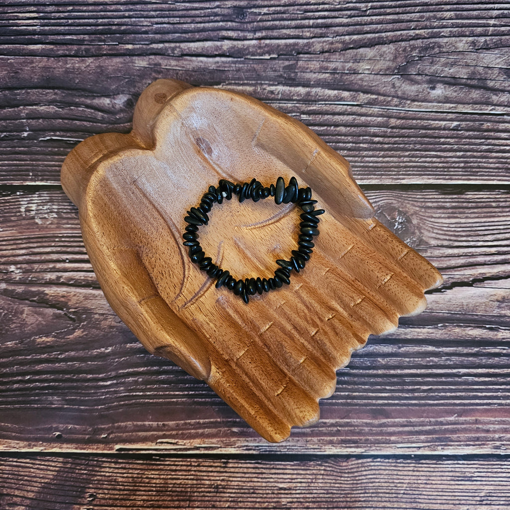 A black chipped Shungite bracelet lays on a pair of wooden hands