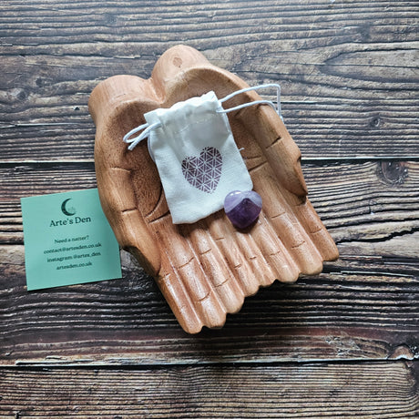 An amethyst crystal heart with matching white bag on a pair of wooden hands. 