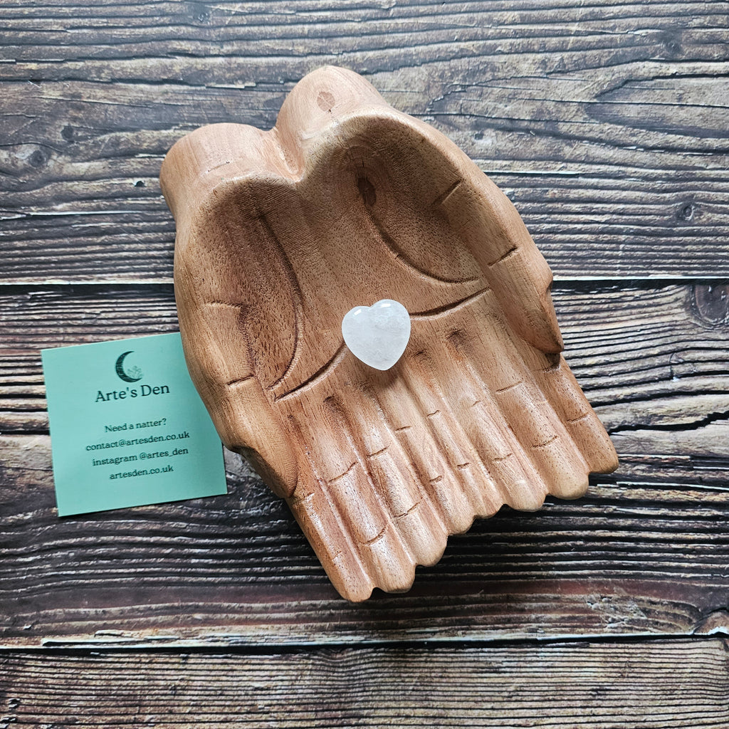 A clear quartz crystal heart stone placed on a wooden pair of hands.