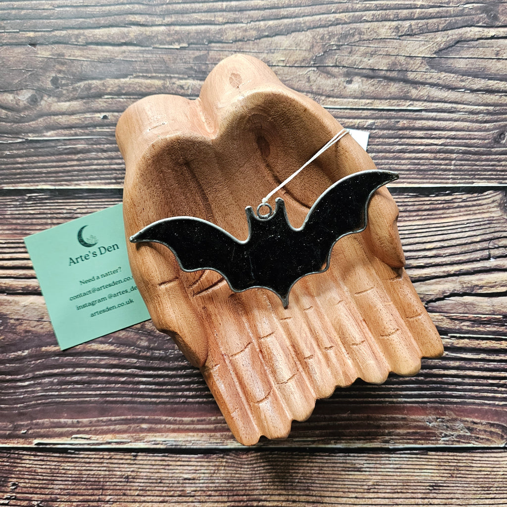A black sparkly bat suncatcher on a pair of wooden hands. 