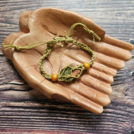A sand-coloured crystal cord bracelet with an example crystal inside, on a pair of wooden hands