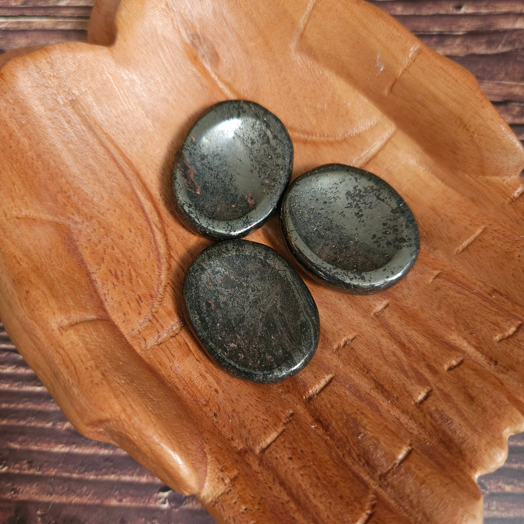 Three grey polished crystal thumbstones resting on a wooden surface