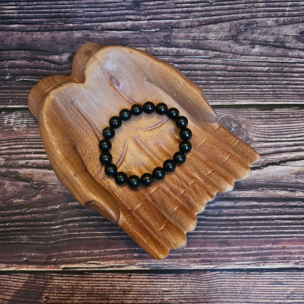 A black beaded Shungite bracelet lays on a pair of wooden hands
