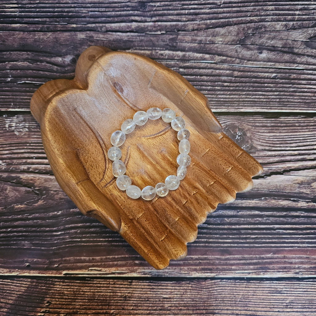 A tumbled crystal bracelet, placed on a wooden bracelet holder shaped like a pair of hands.