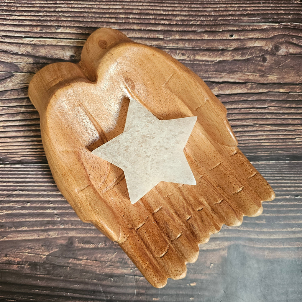 A selenite crystal charging plate shaped as a star, placed on a wooden pair of hands