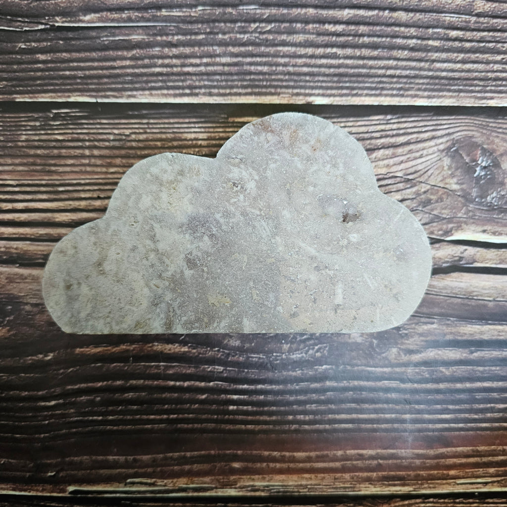 A carved Pink Amethyst crystal shaped as a cloud laid on a wooden background
