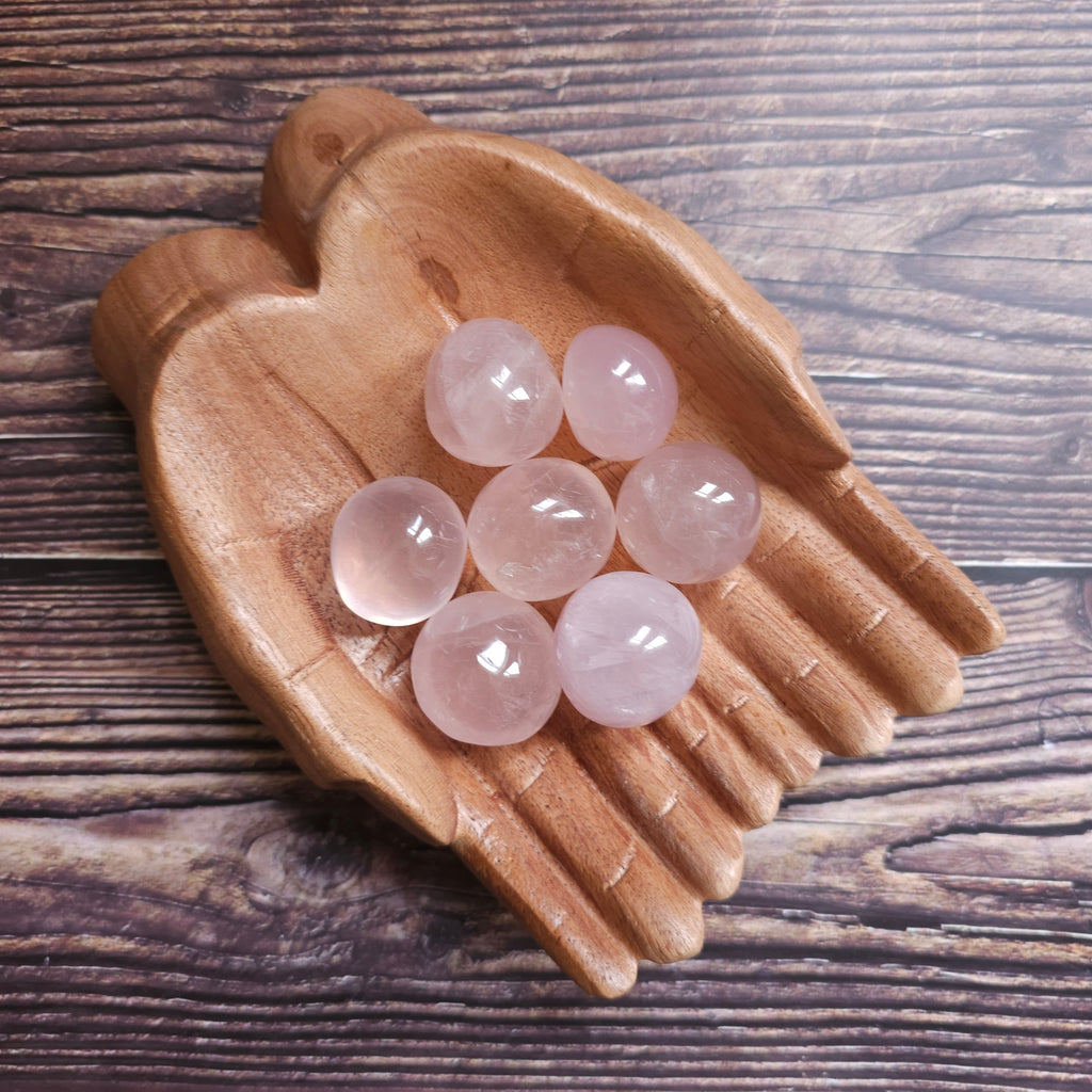 A collection of round rose quartz tumblestones placed on a wooden dish.