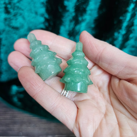 Two carved green aventurine crystal figures shaped like Christmas trees held in a person's hand.
