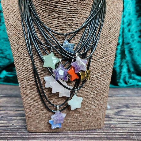 Several star-shaped crystal pendants in various colours displayed on a brown mannequin, with a black cord.