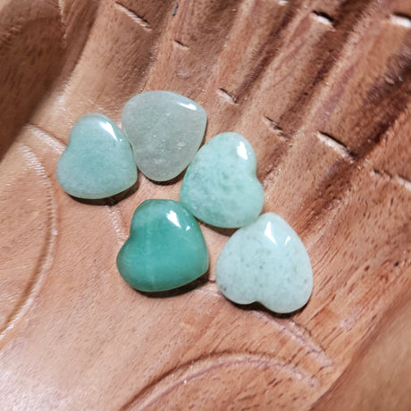 A collection of polished, carved crystal hearts in various shades of green, placed on a wooden surface.