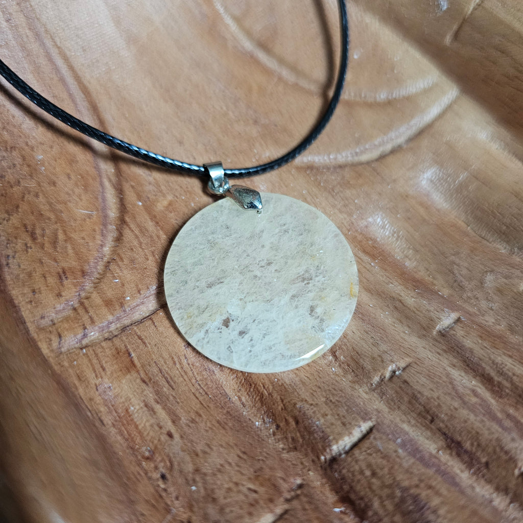 A coin-shaped crystal citrine pendant, attached to a black cord, displayed on a wooden pair of hands