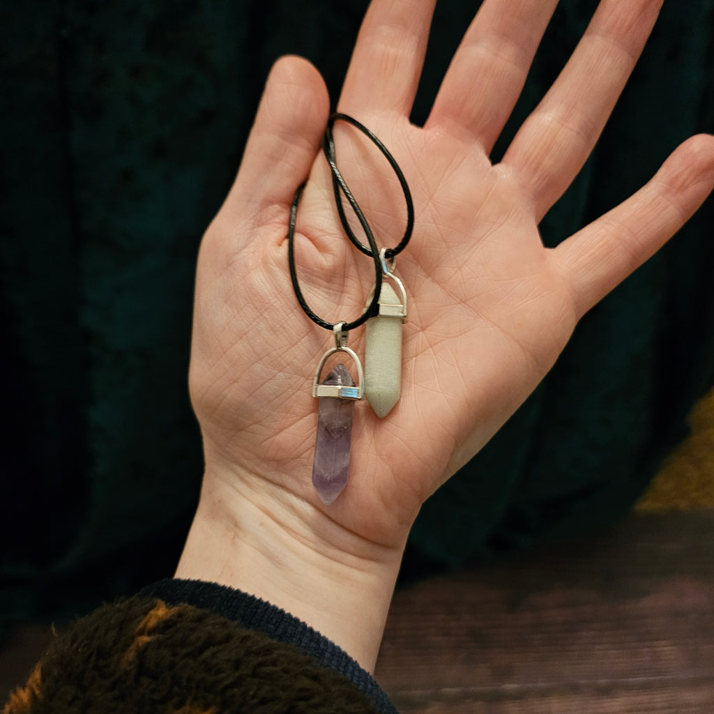 A hand holding two crystal pendant necklaces with black cord