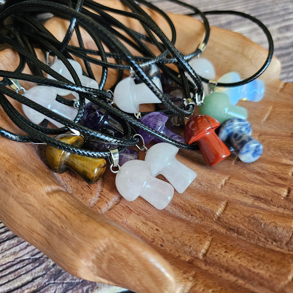 A collection of mushroom-shaped crystal pendants in various colours attached to black cords, held in a pair of wooden hands