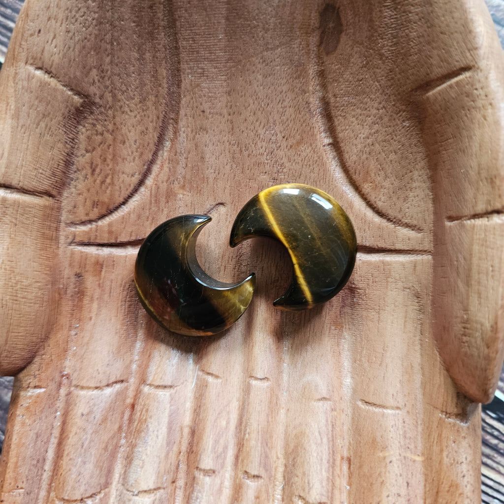 Two carved crescent moon gold-brown banded Tiger's Eye crystals placed on a pair of wooden hands