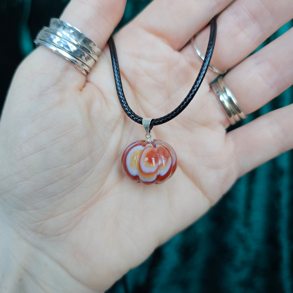 A pumpkin-shaped carnelian crystal pendant attached to a black cord necklace, held in someone's hand