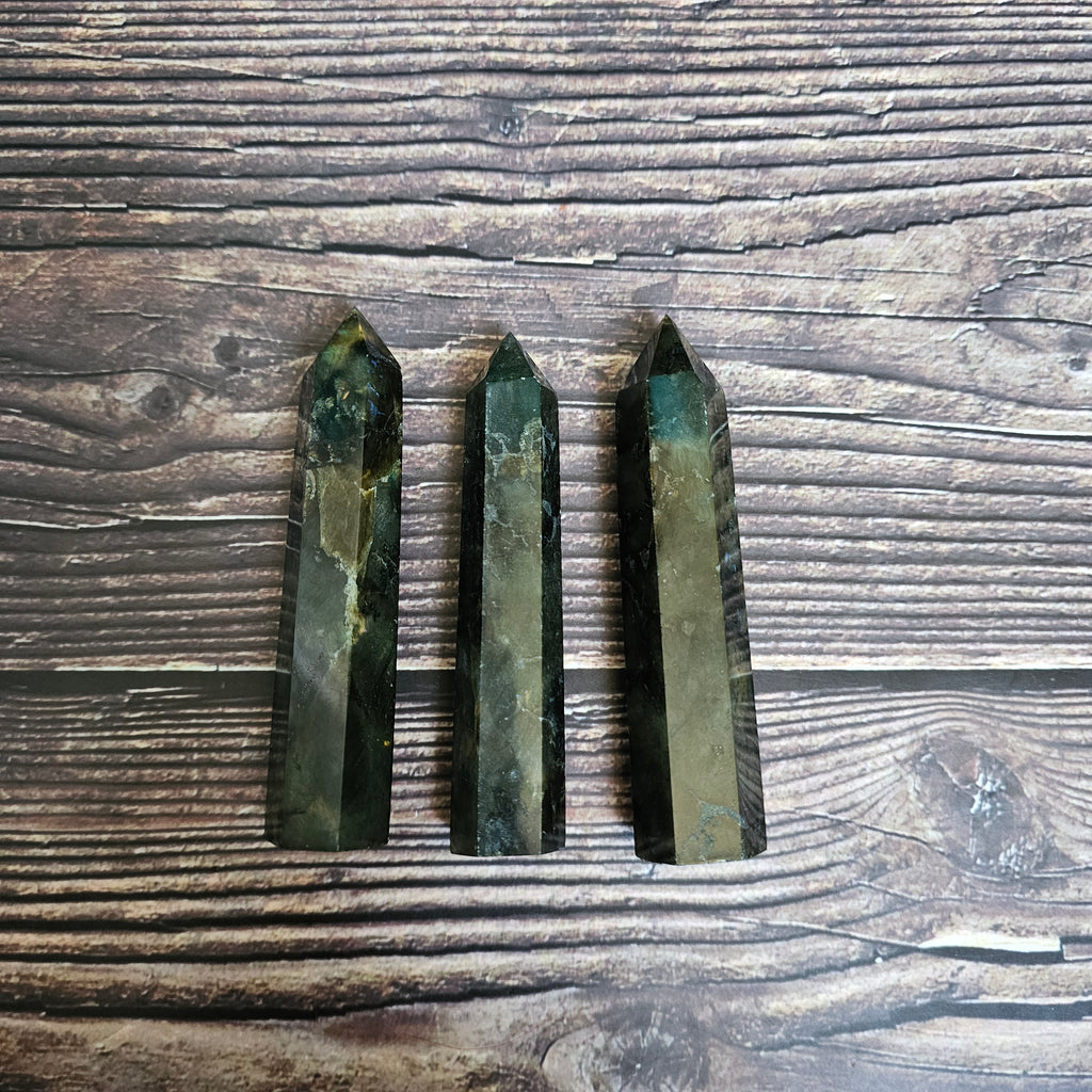 Three Labradorite general crystals lay side by side on a wooden surface. 
