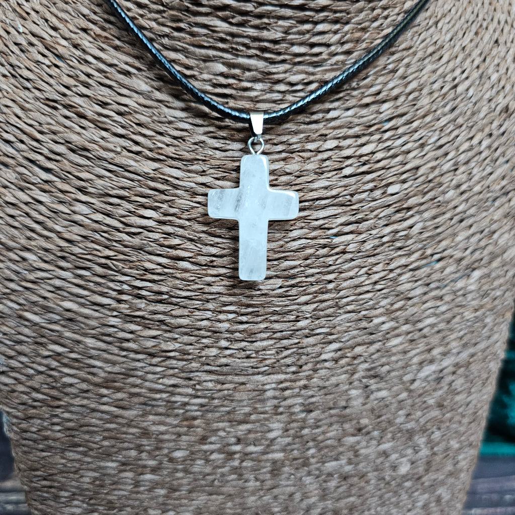 A cross-shaped crystal pendant with a black cord necklace displayed on a textured background.
