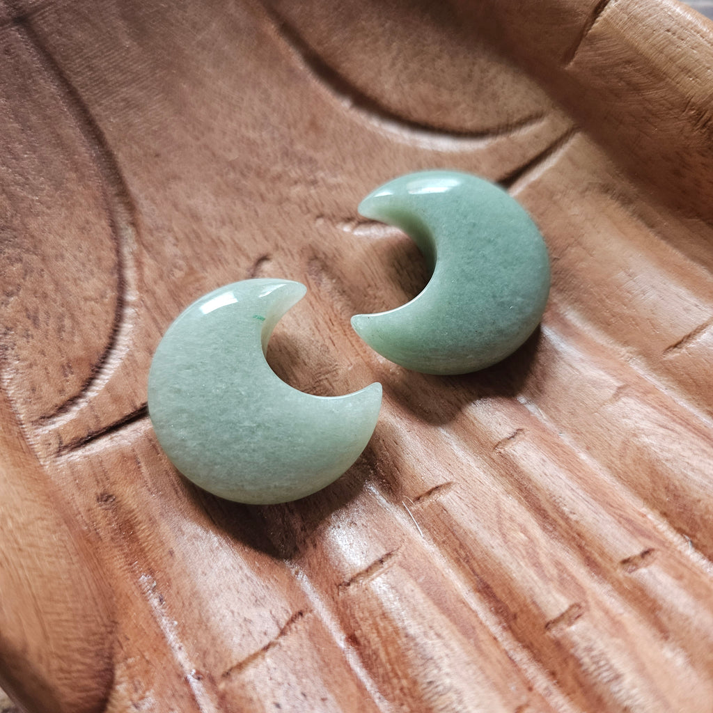 A close up of two green aventurine crescent moon shaped crystals displayed in a pair of wooden hands 