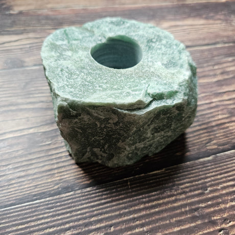 A chunky rough, green aventurine stone tealight holder placed on a wooden surface.