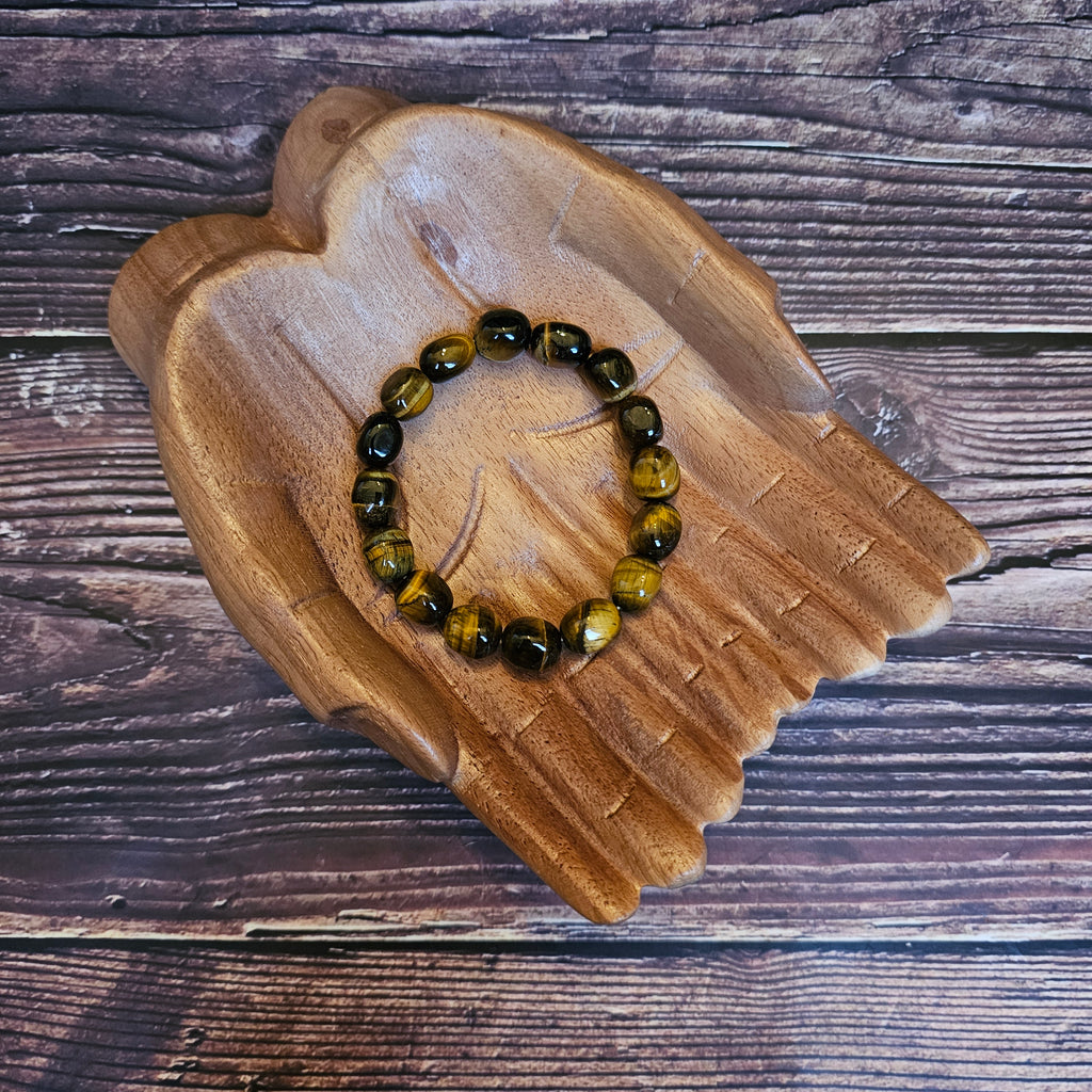 A tumbled crystal bracelet in shades of browns and golds, placed on a wooden bracelet holder shaped like a pair of hands.