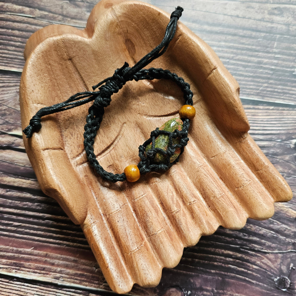 A black-coloured crystal cord bracelet laid on a pair of wooden hands with an example crystal inside