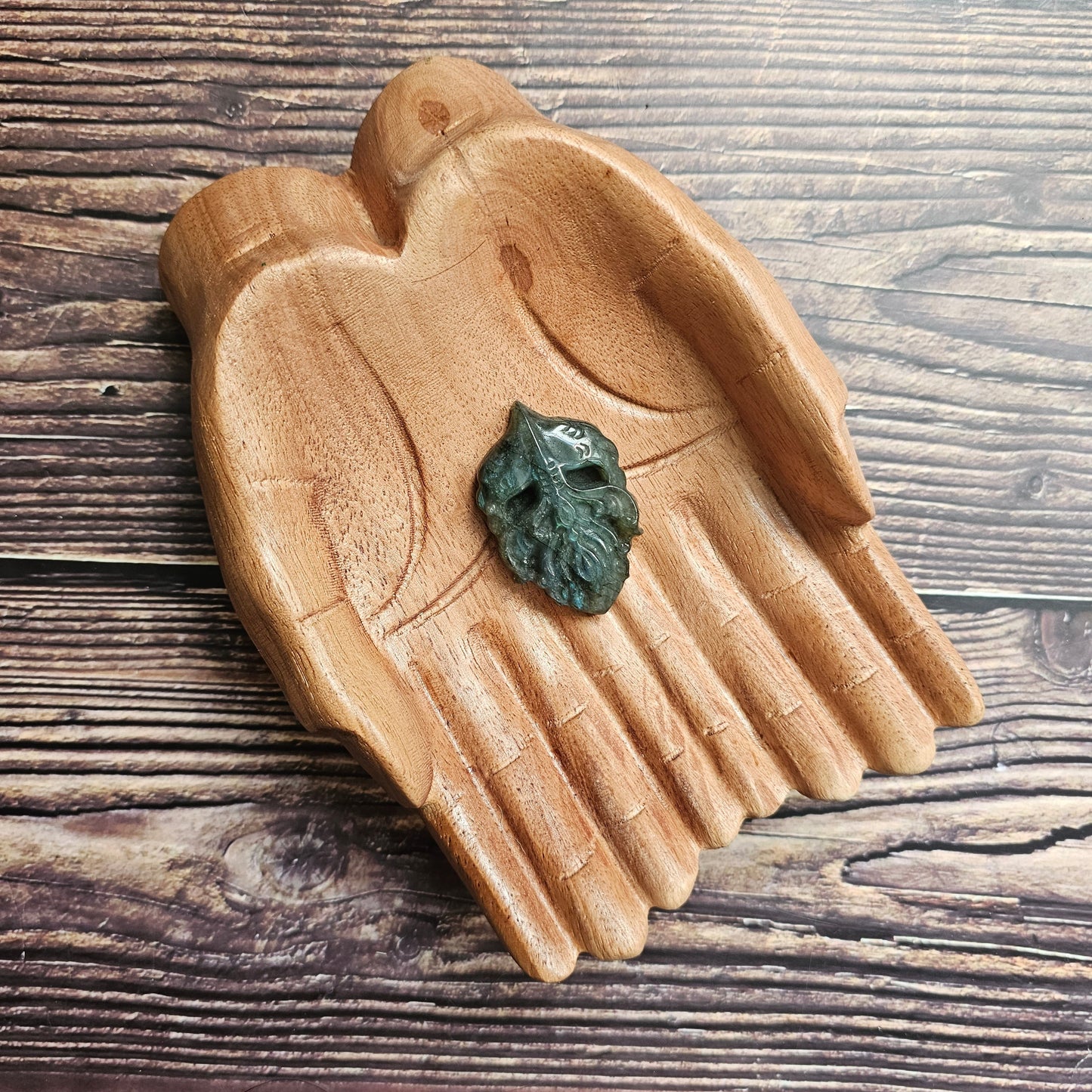 A labradorite viking carving (head) sitting in a pair of wooden hands.