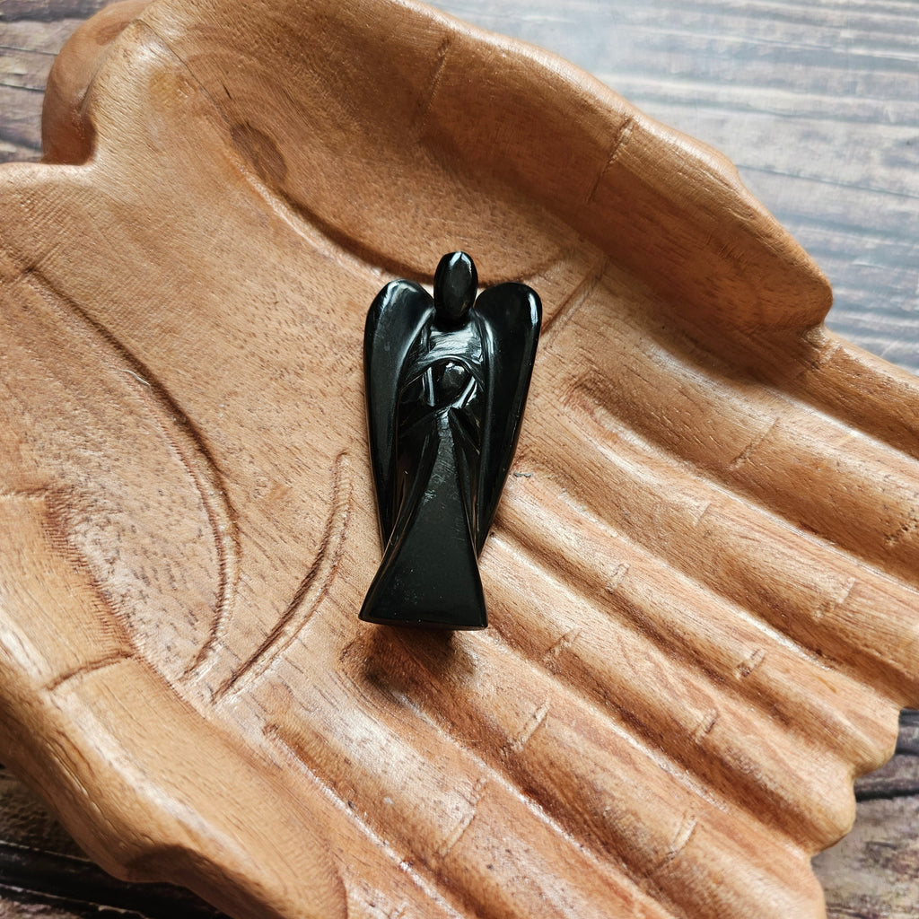 A carved crystal angel figurine placed inside a wooden hand-shaped bowl.
