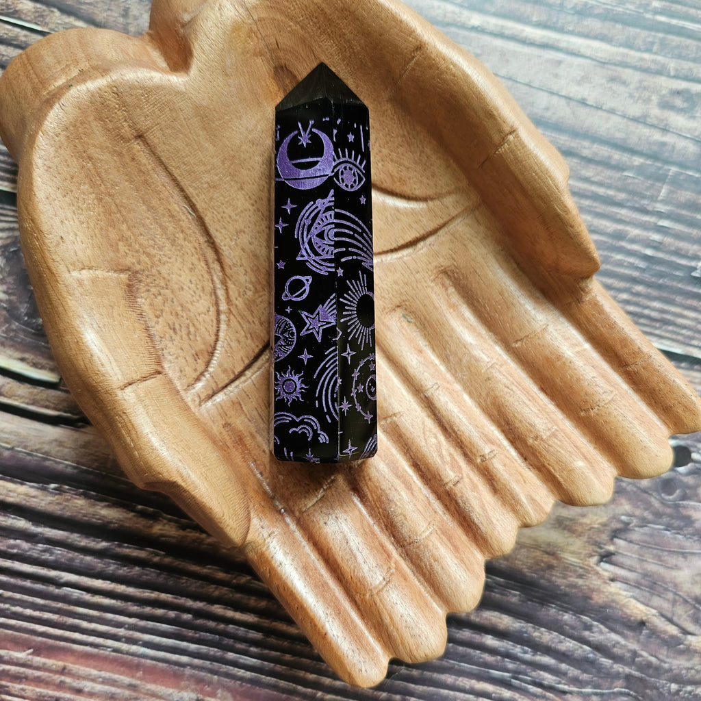 A Black Obsidian Generator with celestial designs displayed on a wooden hand-shaped tray.