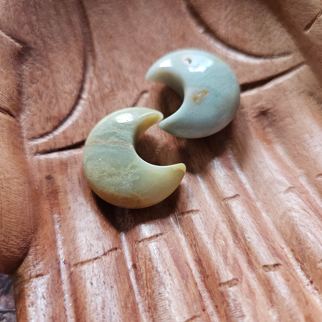 Two amazonite crescent moon shaped crystals placed on a pair of wooden hands