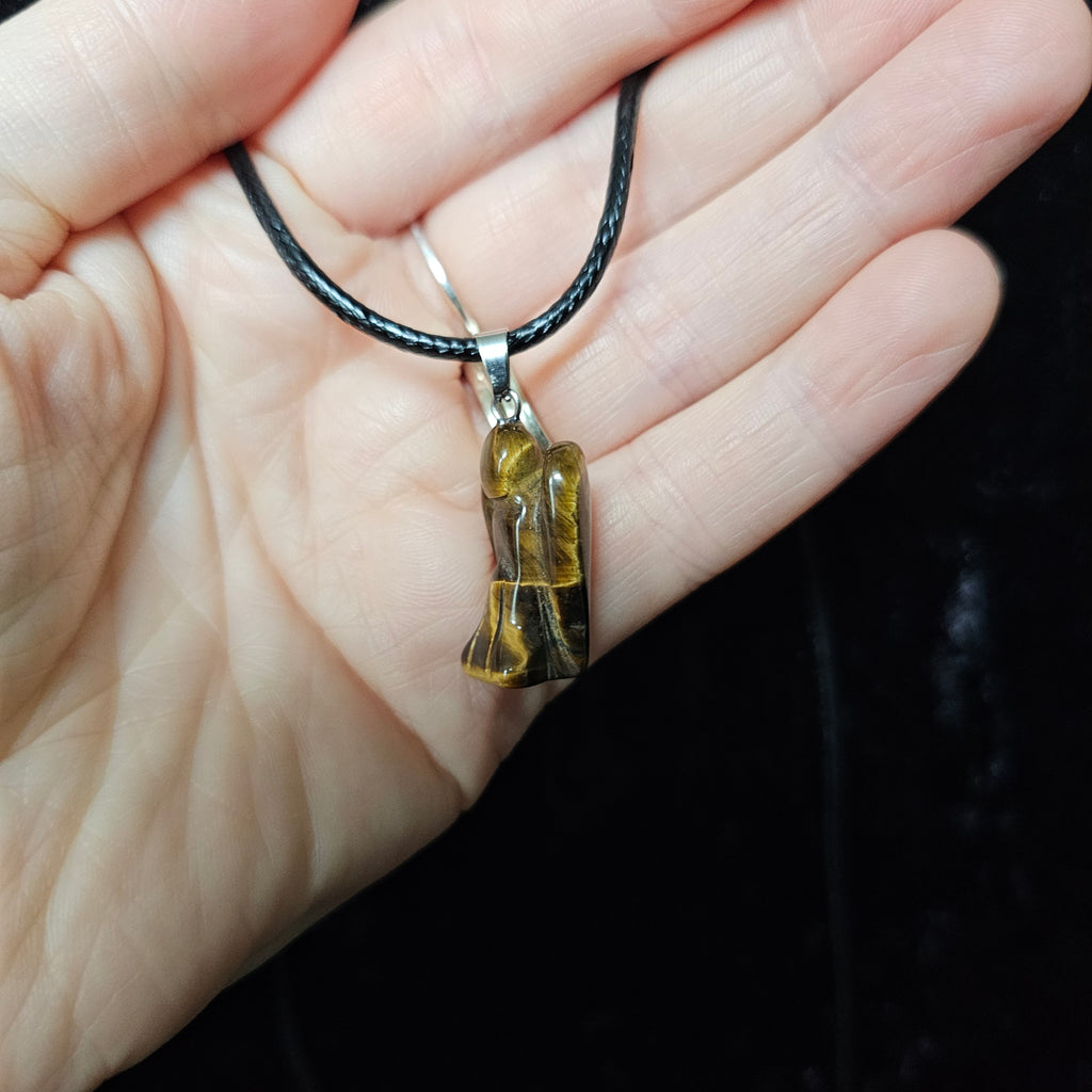 An angel-shaped crystal pendant attached to black cord necklaces on a dark background