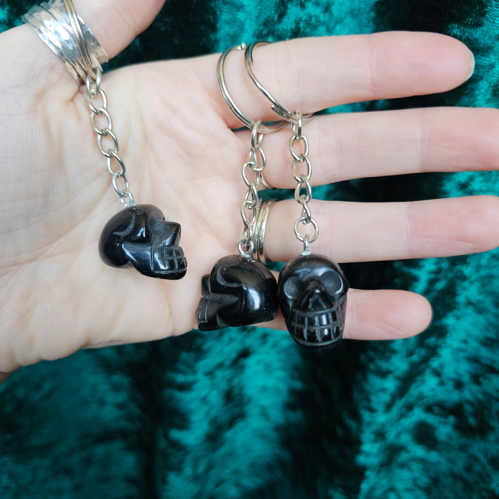 Three Black Obsidian carved crystal skull key chains in someone's hand