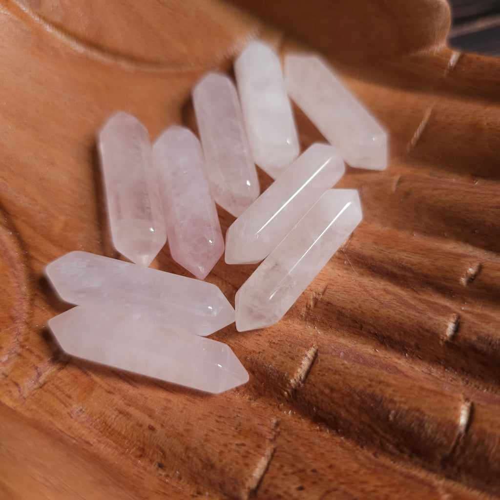 Small pink double pointed crystals held in wooden carved hands