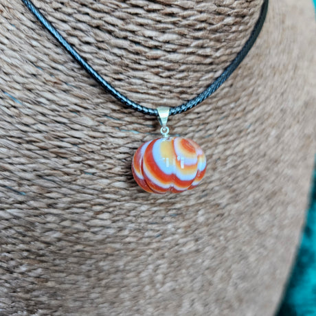 A pumpkin-shaped carnelian crystal pendant attached to a black cord necklace, displayed on a textured background.