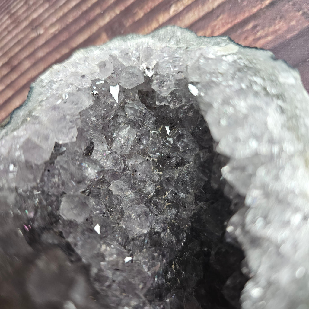 A close up of a rough, opaque purple Amethyst crystal in a standing cluster shape on a wooden surface.