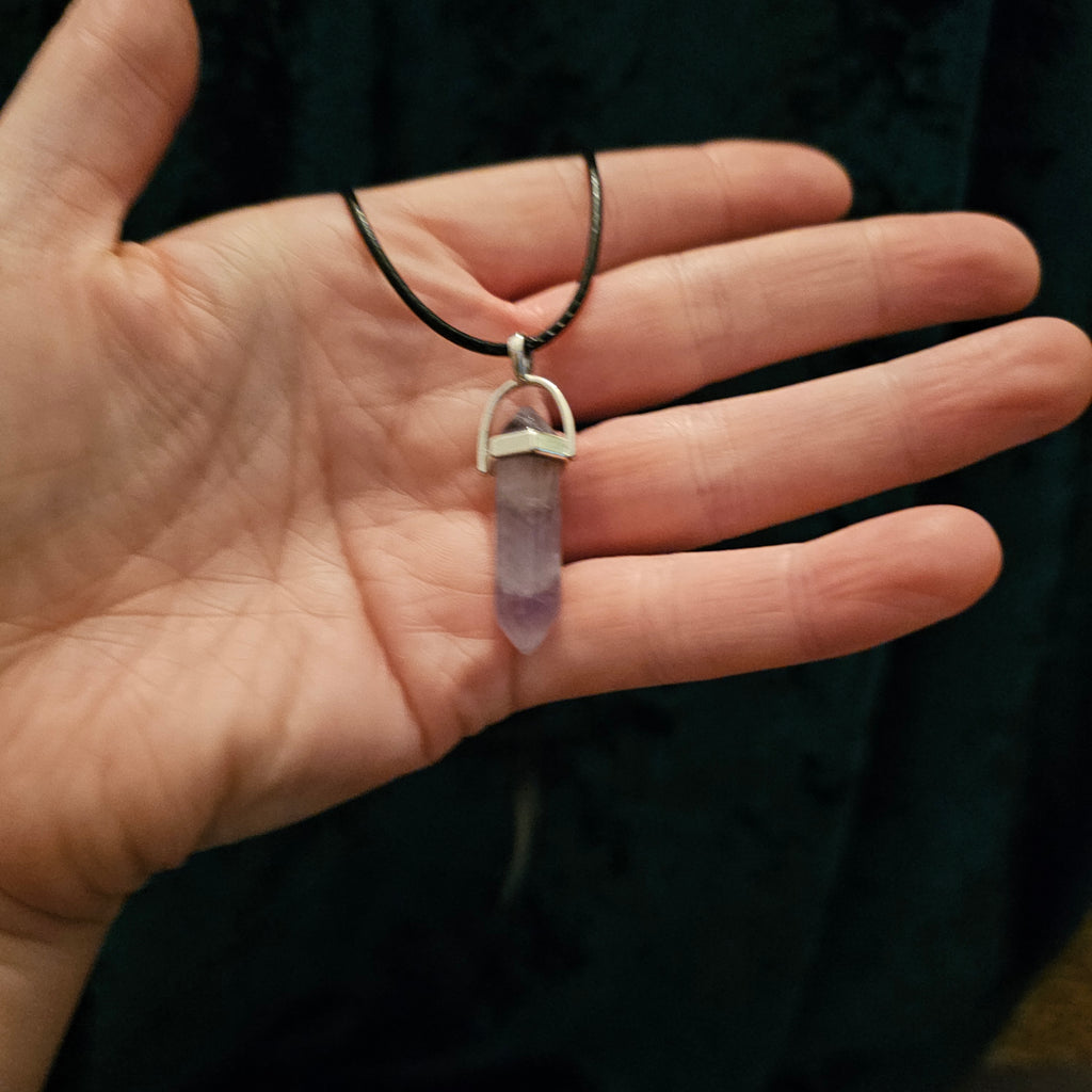 A hand holding a crystal pendant necklace with black cord