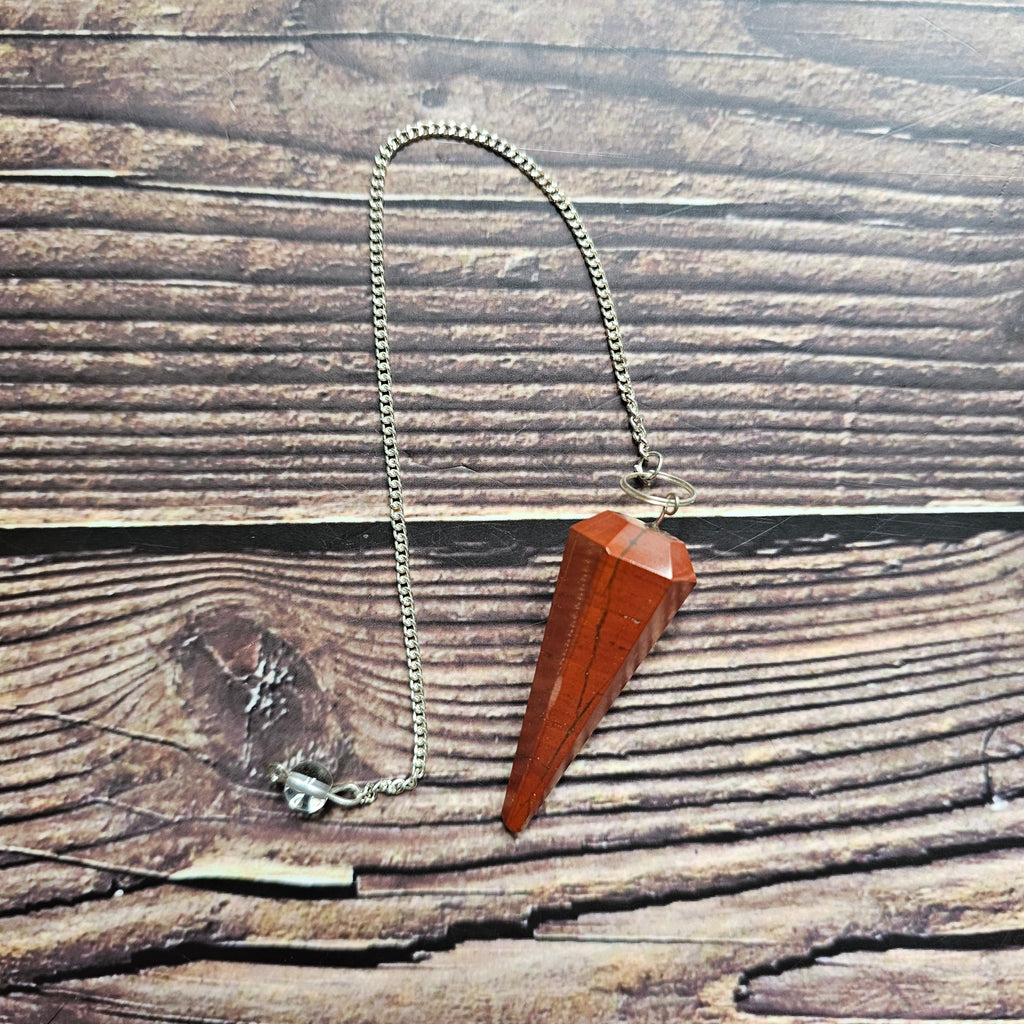 A red jasper pendulum with a silver chain, placed in a wooden hand-shaped dish, on a wooden background.