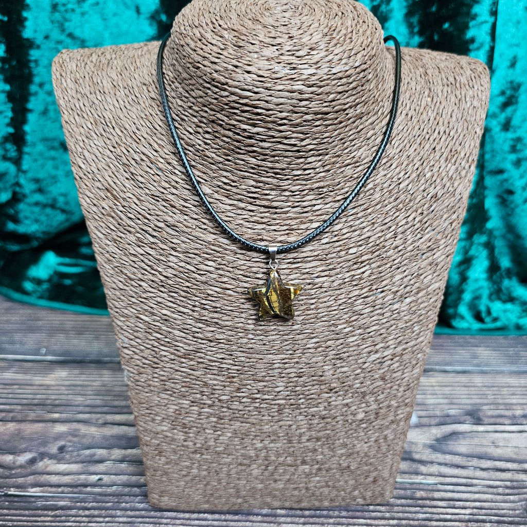 A star-shaped crystal pendant displayed on a brown mannequin, with a black cord.