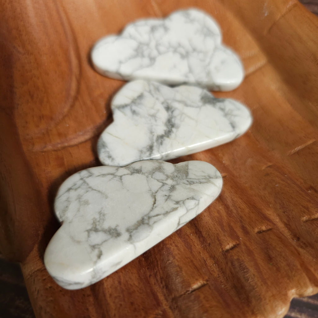 Carved Howlite crystals shaped like clouds, placed on a wooden surface.