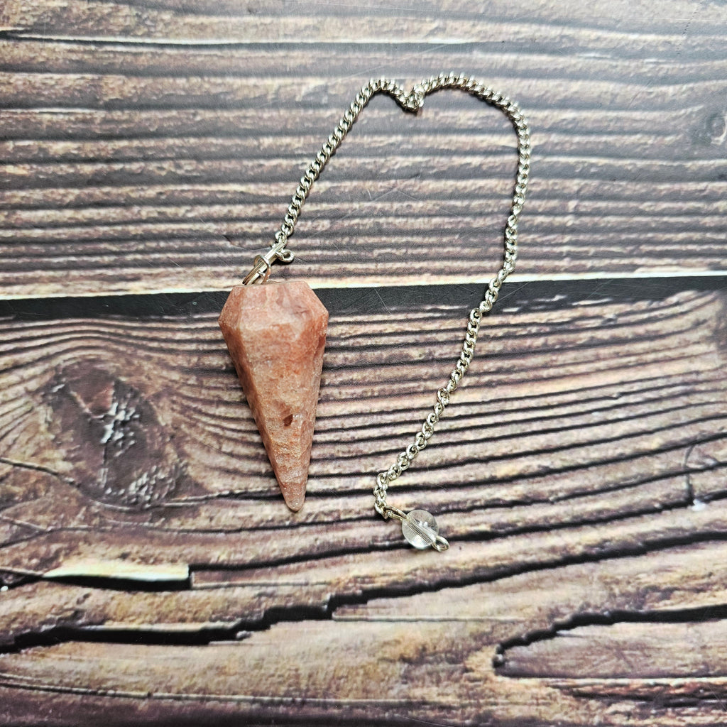 A sunstone pendulum, displayed on a wooden surface.