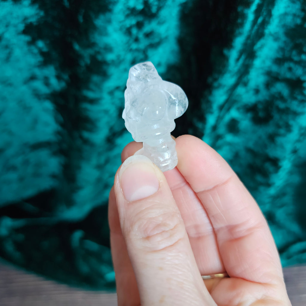 A carved clear quartz crystal Santa figure held in a person's hand.