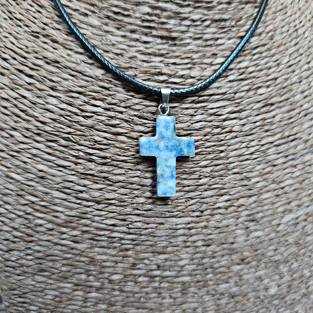 A cross-shaped crystal pendant with a black cord necklace displayed on a textured background.