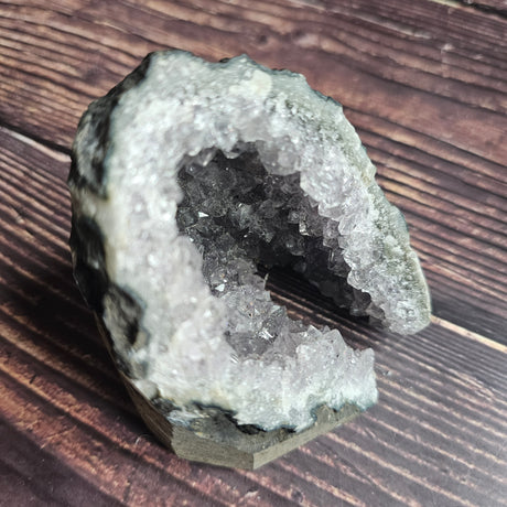 A rough, opaque purple Amethyst crystal in a standing cluster shape on a wooden surface.
